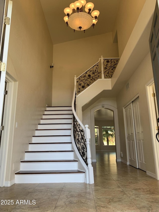staircase with arched walkways, a notable chandelier, visible vents, baseboards, and a towering ceiling