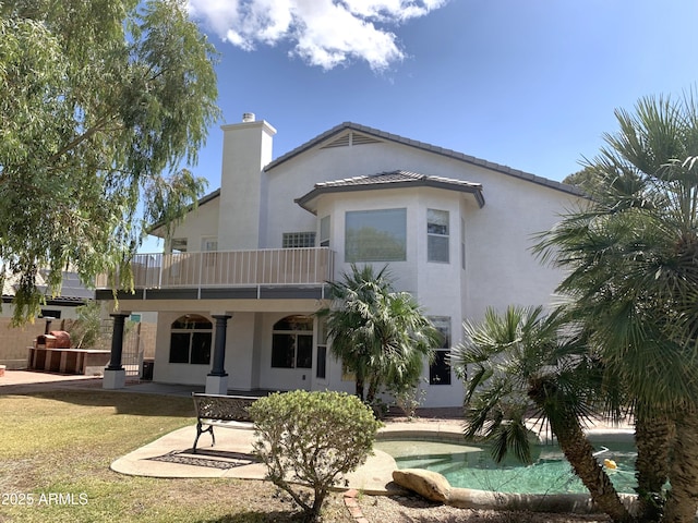 back of property featuring a chimney, a balcony, and stucco siding
