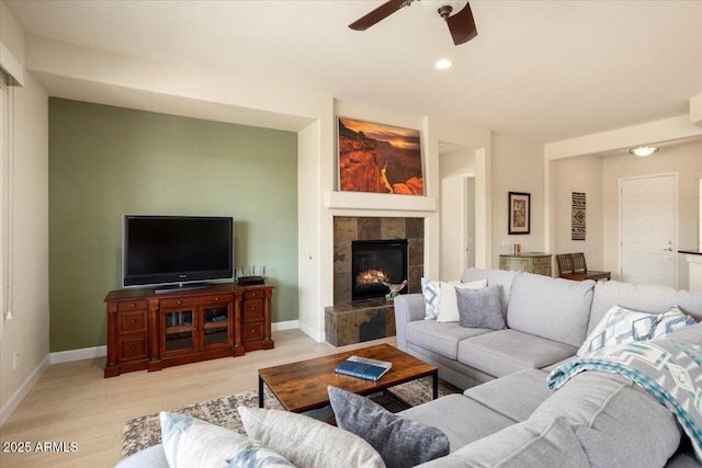 living room featuring a fireplace, ceiling fan, and light wood-type flooring