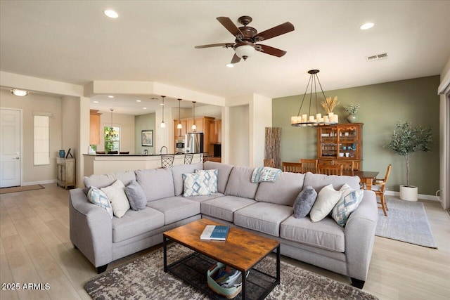 living room with ceiling fan with notable chandelier and light hardwood / wood-style flooring