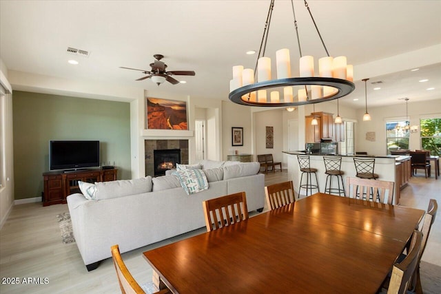 dining space with ceiling fan with notable chandelier, a fireplace, and light wood-type flooring