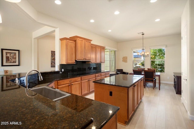 kitchen featuring a kitchen island, sink, dark stone counters, hanging light fixtures, and a notable chandelier