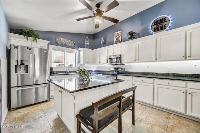 kitchen with appliances with stainless steel finishes, dark stone counters, white cabinets, lofted ceiling, and sink