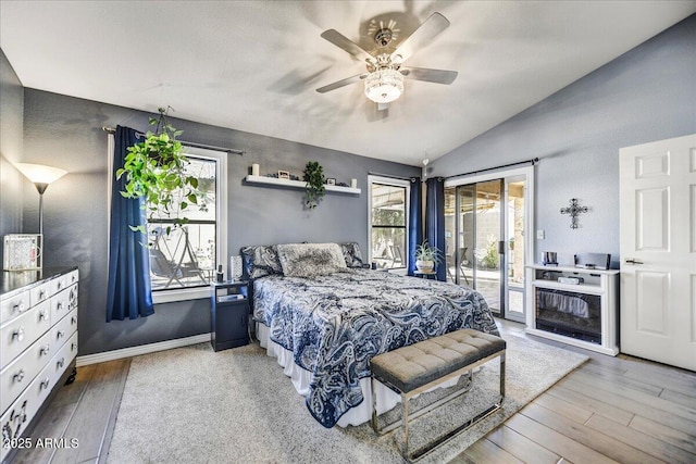 bedroom featuring access to outside, hardwood / wood-style flooring, multiple windows, lofted ceiling, and ceiling fan