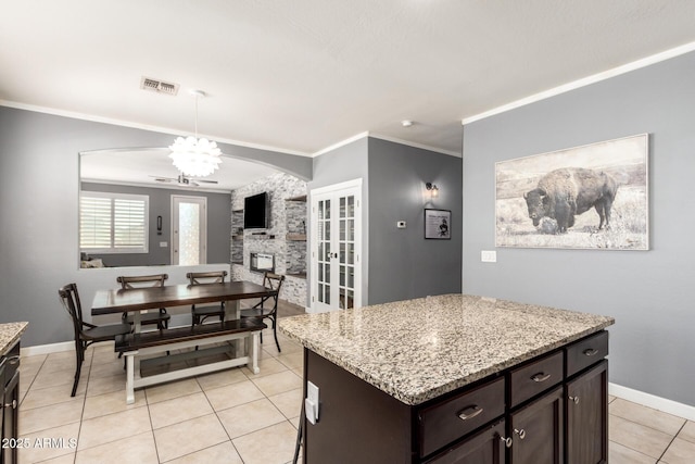 kitchen with dark brown cabinetry, light tile patterned floors, baseboards, light stone countertops, and crown molding