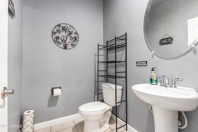 bathroom with a textured wall, tile patterned flooring, toilet, a sink, and baseboards