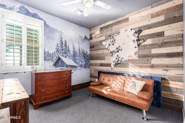 living area featuring wood walls, a ceiling fan, visible vents, and carpet flooring