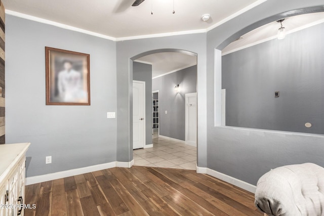 corridor with arched walkways, crown molding, baseboards, and wood finished floors