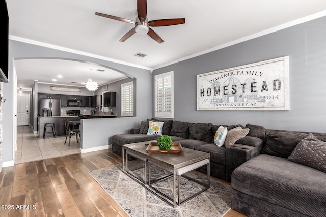 living area with arched walkways, visible vents, baseboards, light wood finished floors, and crown molding