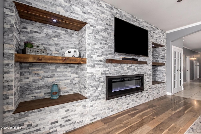 unfurnished living room with ornamental molding, wood finished floors, and a glass covered fireplace