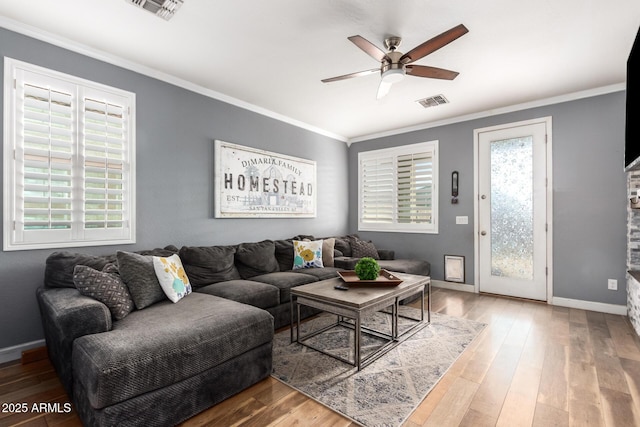 living room with a ceiling fan, baseboards, visible vents, wood-type flooring, and crown molding