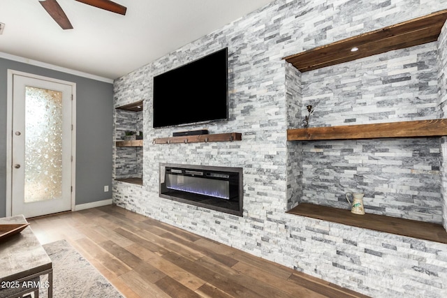 unfurnished living room featuring a stone fireplace, wood finished floors, a ceiling fan, baseboards, and crown molding