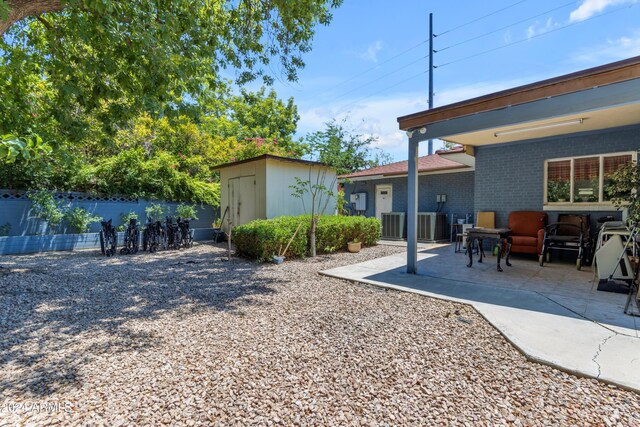 view of yard with central air condition unit, a storage shed, a patio area, fence, and an outdoor structure