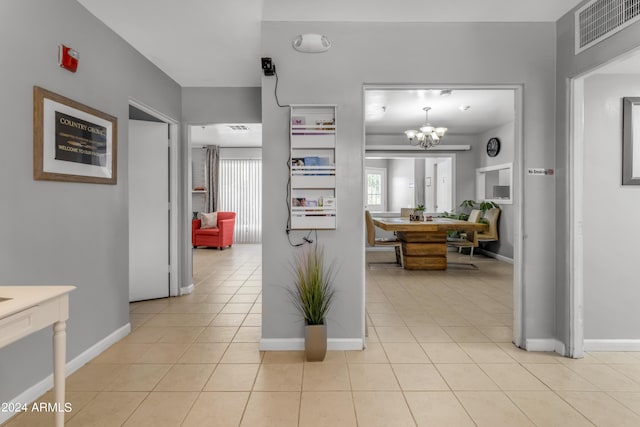 hall featuring light tile patterned floors, baseboards, visible vents, and a notable chandelier