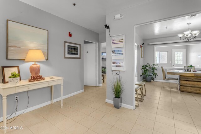 corridor featuring baseboards, an inviting chandelier, and light tile patterned floors