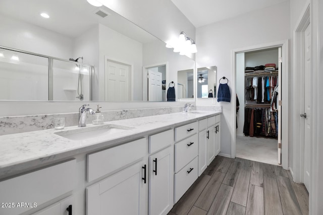 full bath with visible vents, double vanity, a stall shower, a sink, and a walk in closet