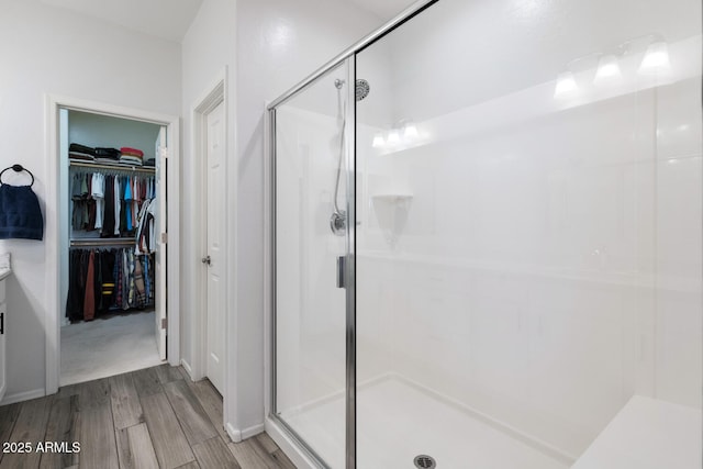 full bath featuring a stall shower, a walk in closet, and wood finished floors