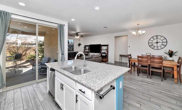 kitchen with wood finish floors, a sink, stainless steel dishwasher, open floor plan, and white cabinets