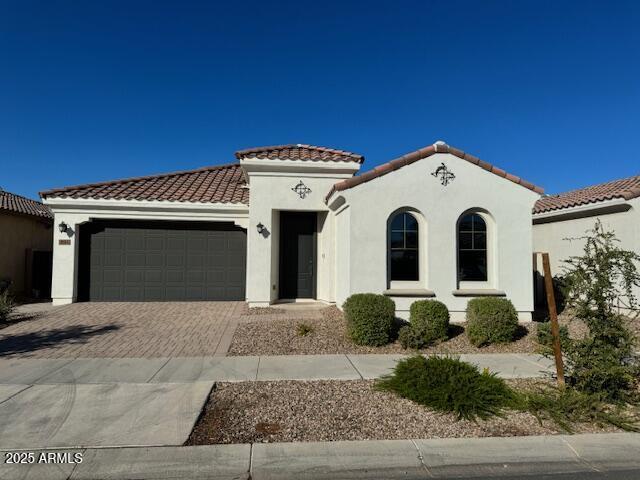 mediterranean / spanish-style home featuring a garage, a tile roof, stucco siding, and driveway