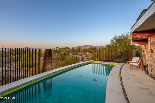 pool at dusk featuring a mountain view and a patio