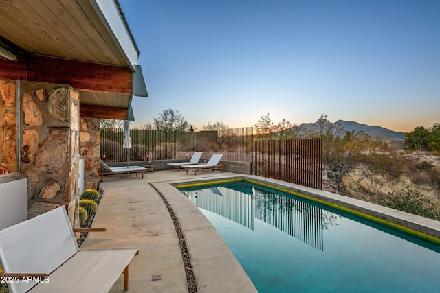 pool at dusk featuring a mountain view and a patio area