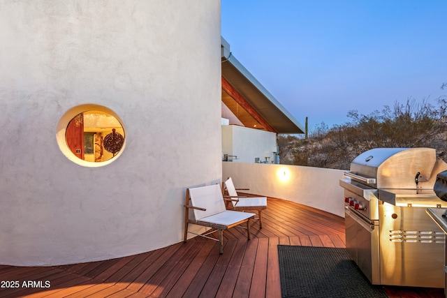 deck at dusk featuring an outdoor kitchen and a grill