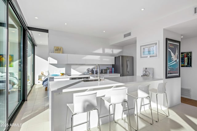 kitchen with sink, light tile patterned floors, stainless steel fridge, a kitchen breakfast bar, and white cabinets