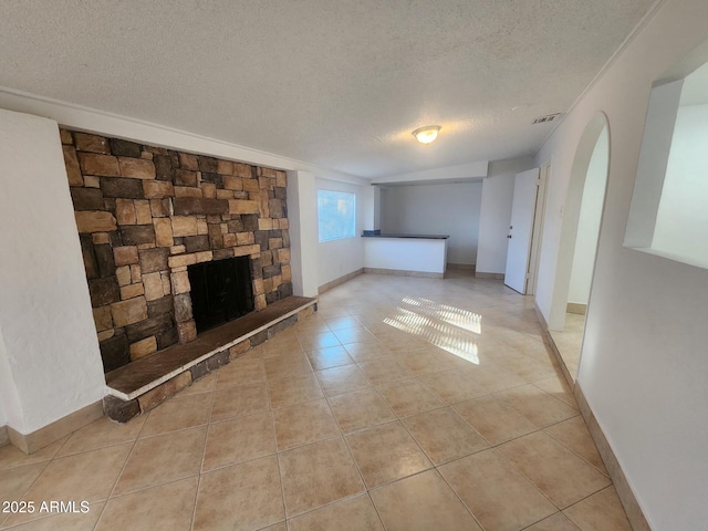 unfurnished living room featuring a stone fireplace, light tile patterned floors, and a textured ceiling