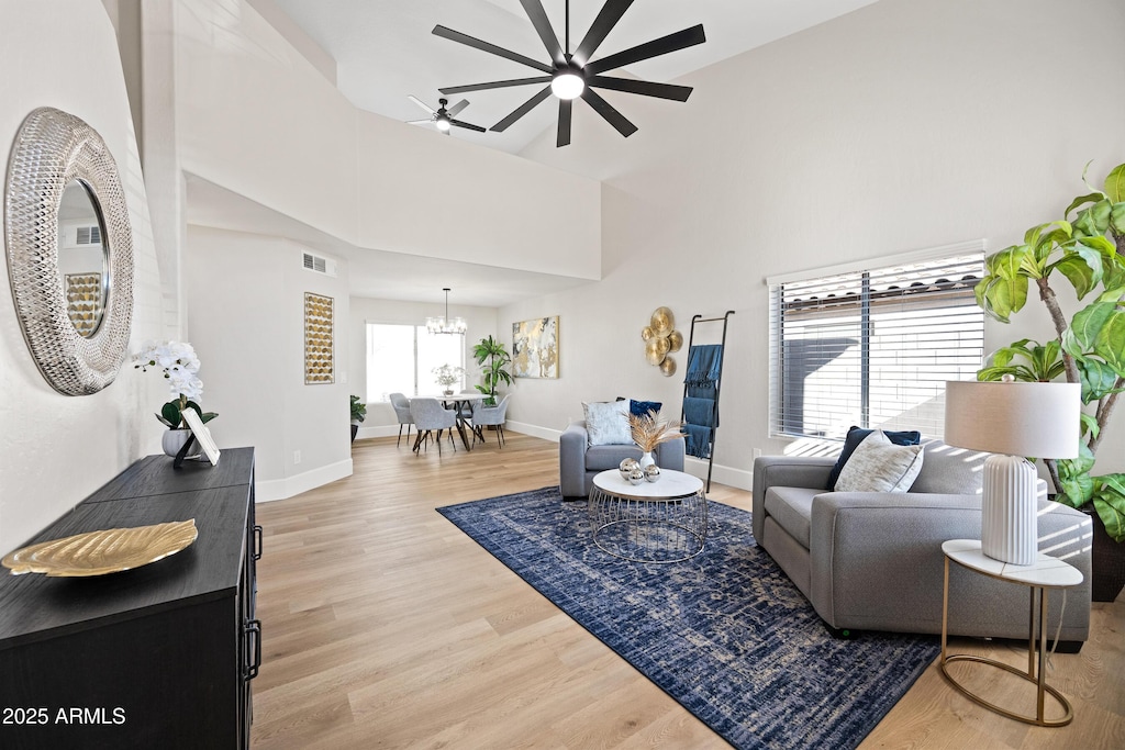 living room with ceiling fan with notable chandelier, light hardwood / wood-style flooring, and a towering ceiling