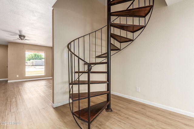 stairs with light hardwood / wood-style floors, a textured ceiling, and ceiling fan