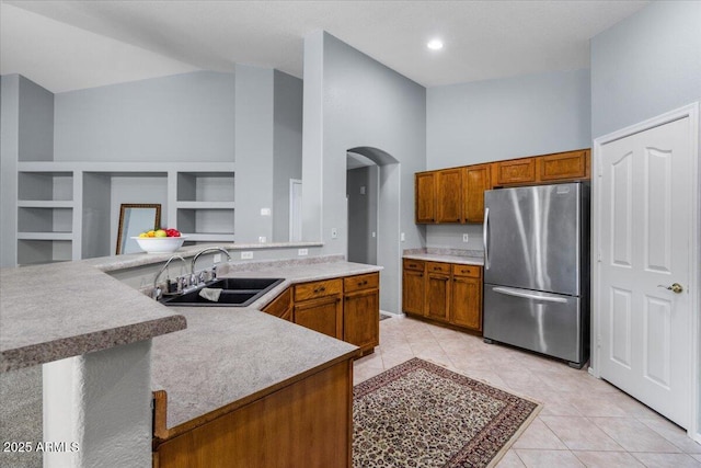 10235 E Jerome Ave, Mesa, AZ 85209 - kitchen featuring freestanding refrigerator, arched walkways, light tile patterned floors, brown cabinetry, and light countertops