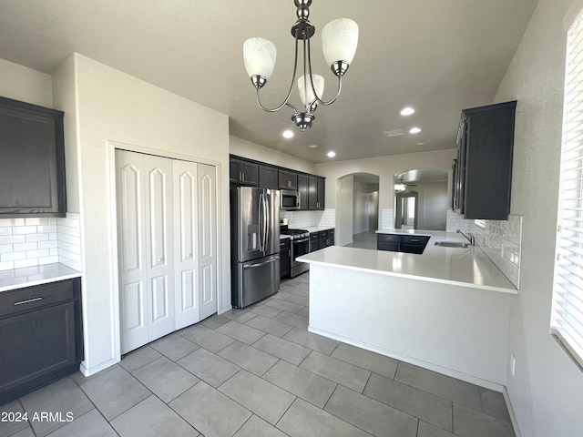 kitchen featuring kitchen peninsula, appliances with stainless steel finishes, backsplash, sink, and decorative light fixtures