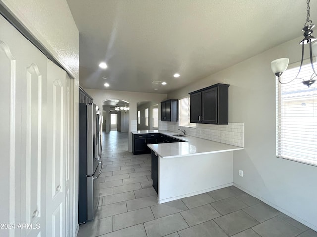 kitchen featuring sink, backsplash, kitchen peninsula, stainless steel fridge, and light tile patterned floors