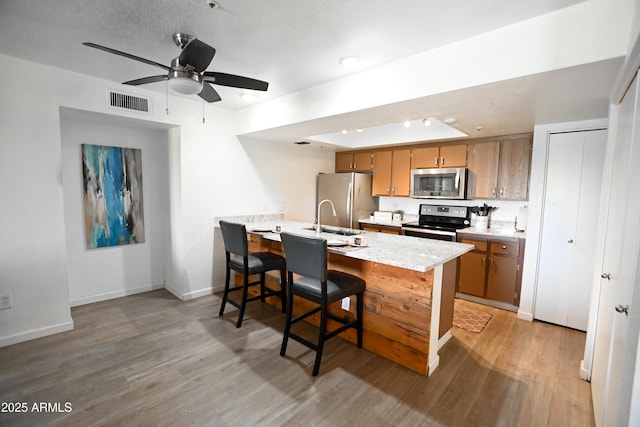7777 E Main St Unit 227, Scottsdale, AZ 85251 - kitchen with appliances with stainless steel finishes, light wood-style floors, a peninsula, brown cabinetry, and a ceiling fan