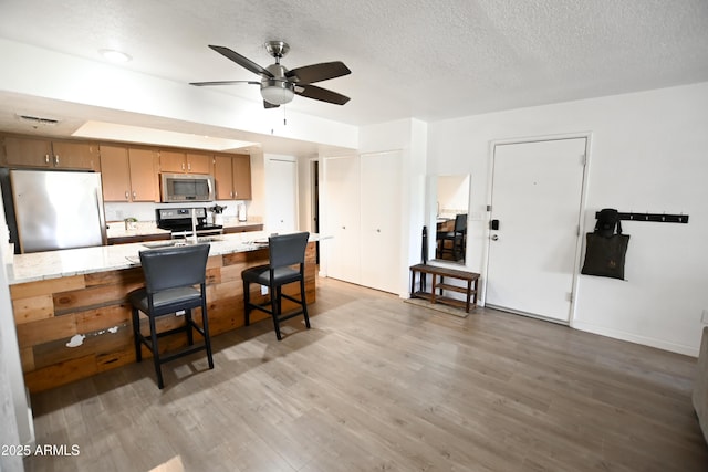 7777 E Main St Unit 227, Scottsdale, AZ 85251 - kitchen with appliances with stainless steel finishes, ceiling fan, light wood-style floors, a textured ceiling, and brown cabinetry
