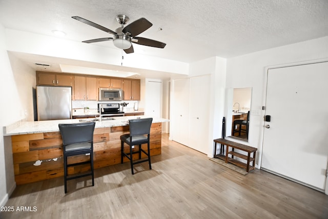 7777 E Main St Unit 227, Scottsdale, AZ 85251 - kitchen featuring appliances with stainless steel finishes, light wood-type flooring, a textured ceiling, a peninsula, and a ceiling fan