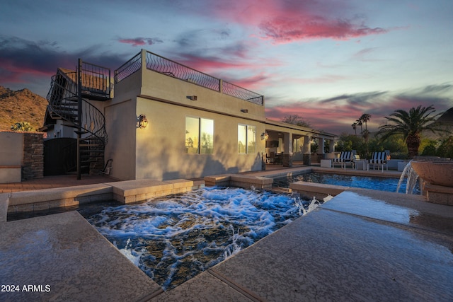 pool at dusk featuring a patio area, pool water feature, and a hot tub