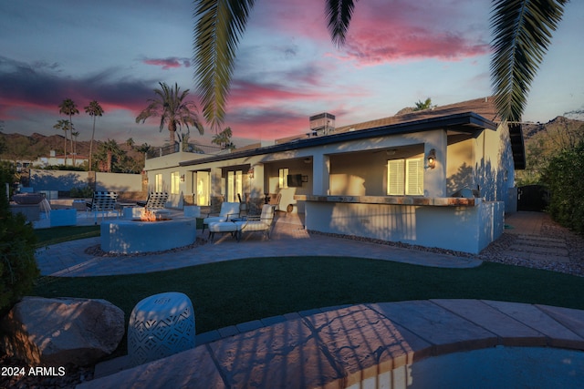 back house at dusk with an outdoor bar, a patio, and a fire pit