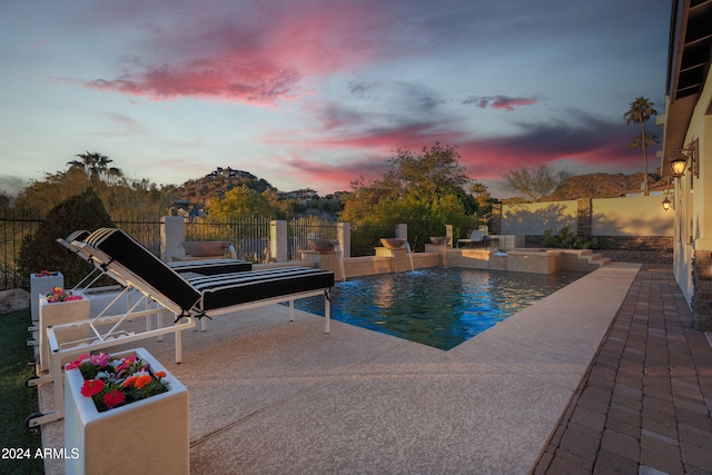 pool at dusk with pool water feature and a patio area