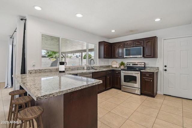 2519 E Geneva Dr, Tempe, AZ 85282 - kitchen featuring stainless steel appliances, a peninsula, dark brown cabinets, a kitchen bar, and light tile patterned floors