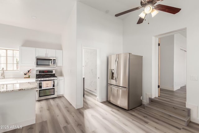 kitchen featuring white cabinets, light stone countertops, stainless steel appliances, and a high ceiling