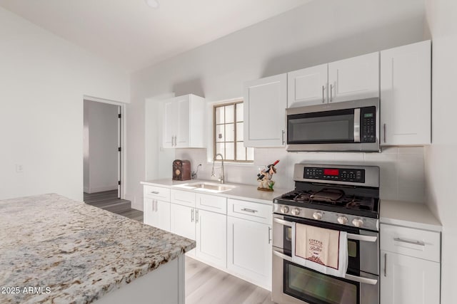 kitchen featuring light stone countertops, sink, stainless steel appliances, light hardwood / wood-style floors, and white cabinets