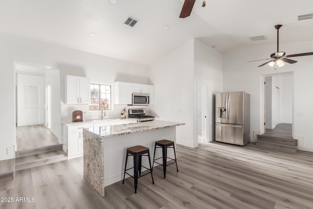 kitchen with stainless steel appliances, a kitchen island, sink, white cabinetry, and lofted ceiling