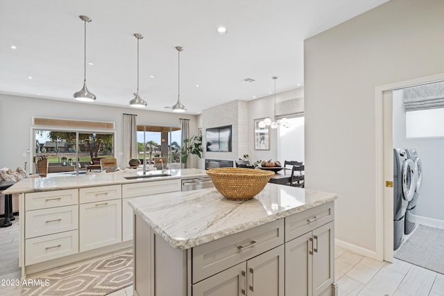 kitchen featuring washing machine and clothes dryer, sink, light stone counters, a kitchen island, and pendant lighting