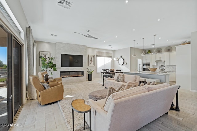 living room featuring ceiling fan, a large fireplace, and light hardwood / wood-style floors