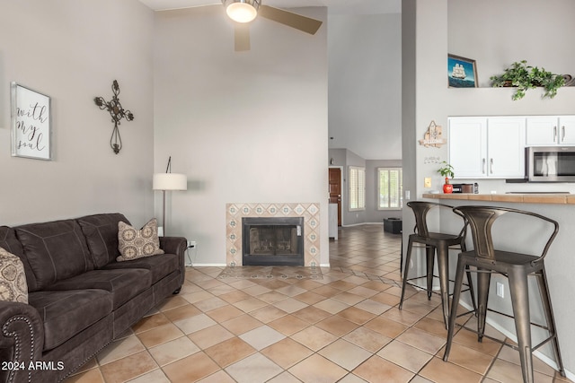 living room featuring a tile fireplace, ceiling fan, high vaulted ceiling, and light tile patterned floors