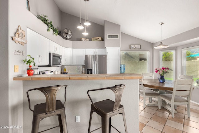 kitchen featuring kitchen peninsula, appliances with stainless steel finishes, a kitchen bar, decorative light fixtures, and white cabinets