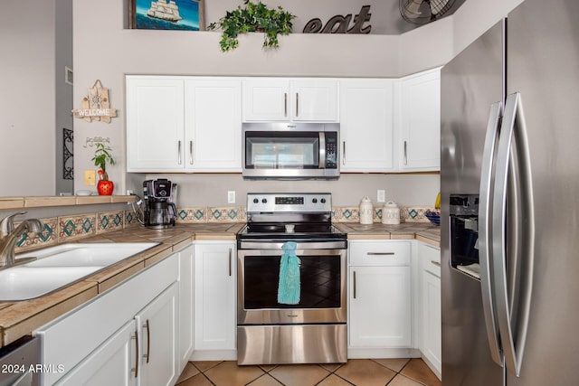 kitchen with tile countertops, white cabinetry, sink, and appliances with stainless steel finishes