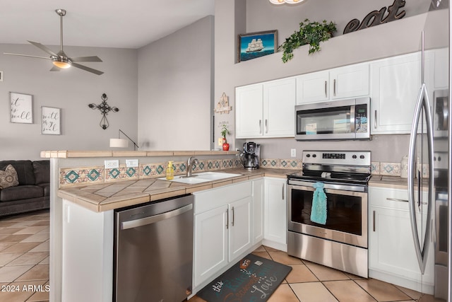 kitchen featuring white cabinetry, sink, kitchen peninsula, tile countertops, and appliances with stainless steel finishes