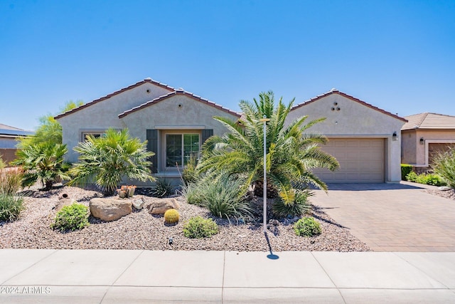 mediterranean / spanish-style house featuring a garage, a tiled roof, decorative driveway, and stucco siding